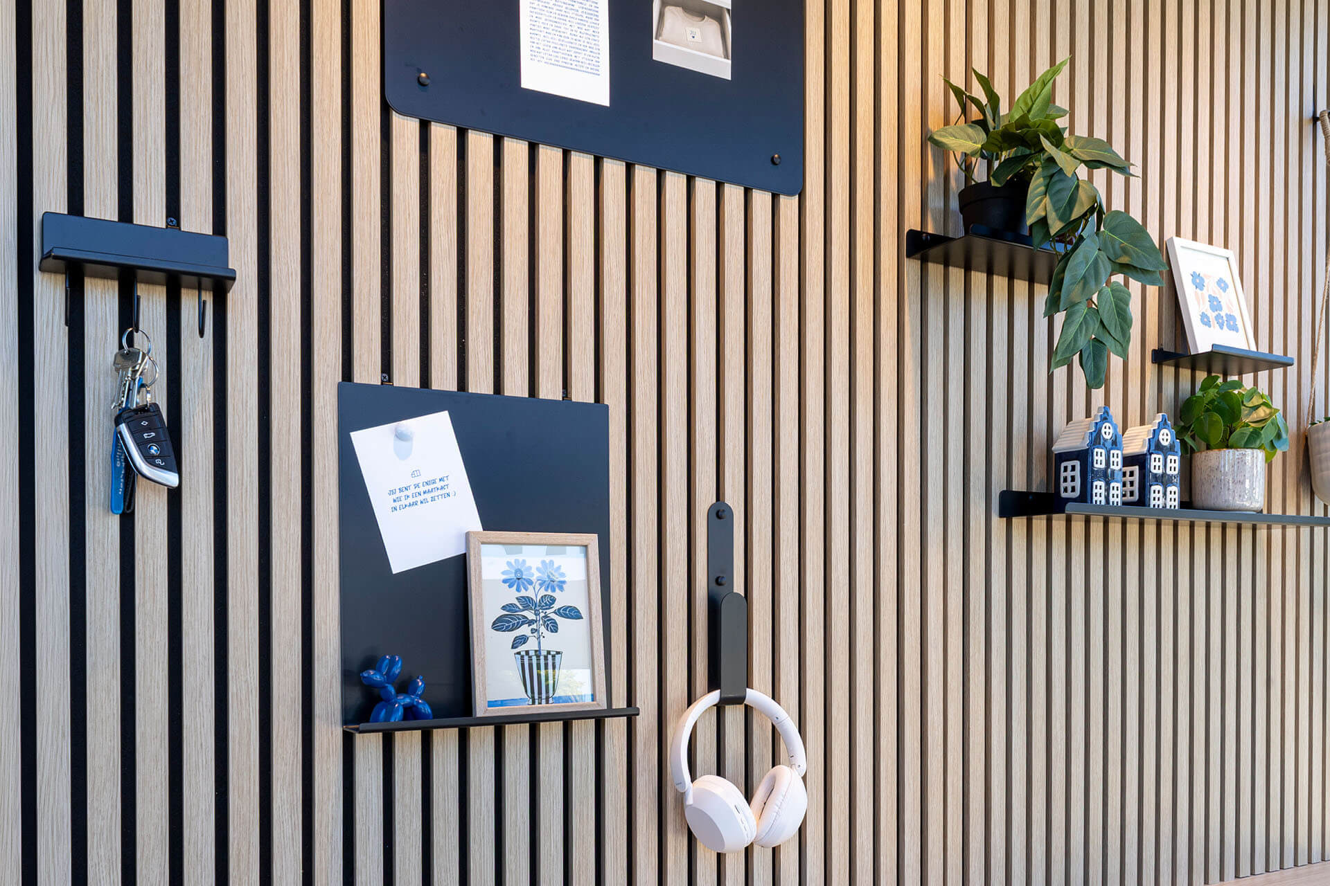 Een muur bekleed met akoestische panelen en accessoires zoals een magneetbord, wandplankjes en handige haakjes 
