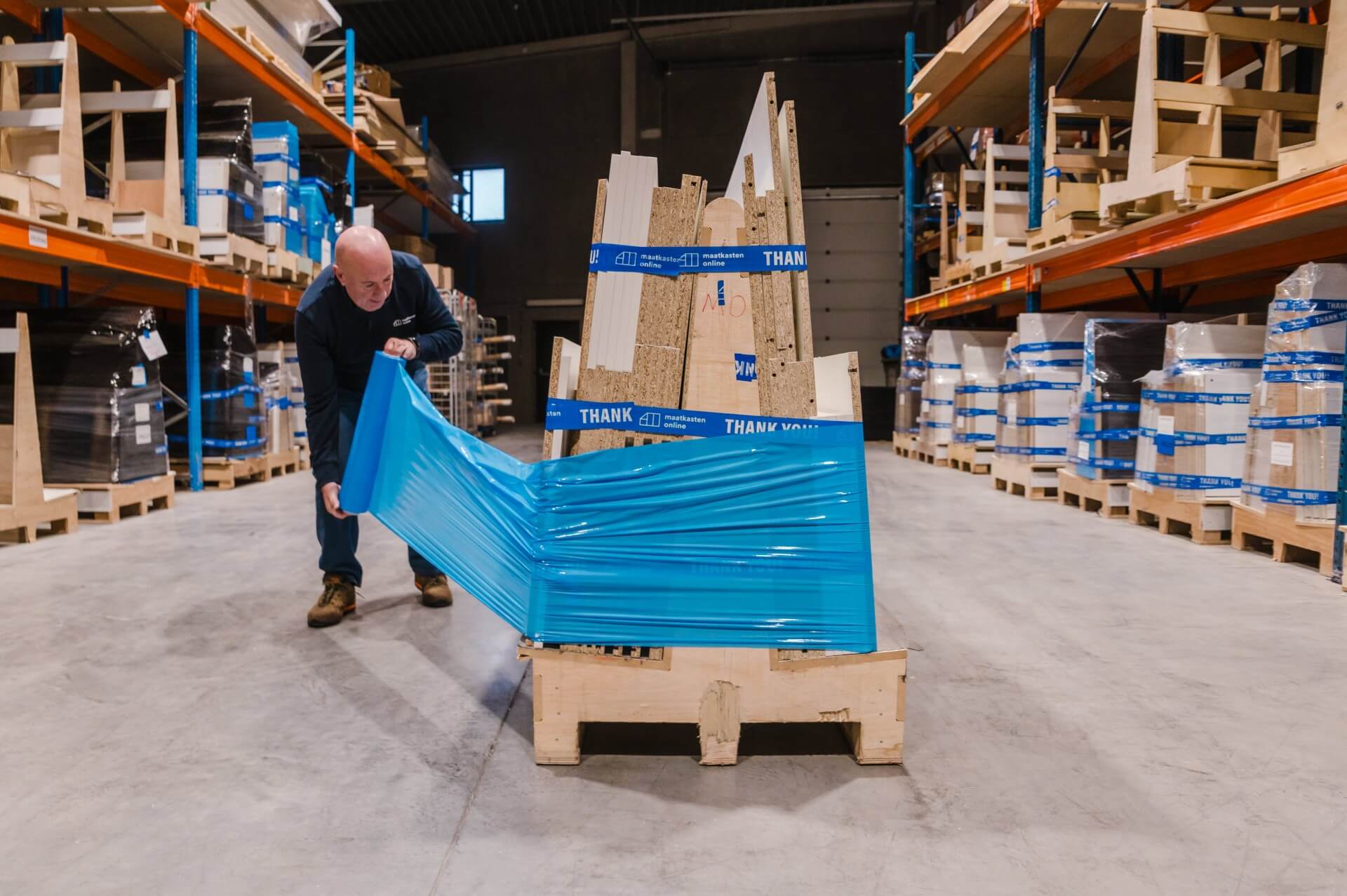 Persoon wikkelt bok met onderdelen van maatkasten in in plastiek folie