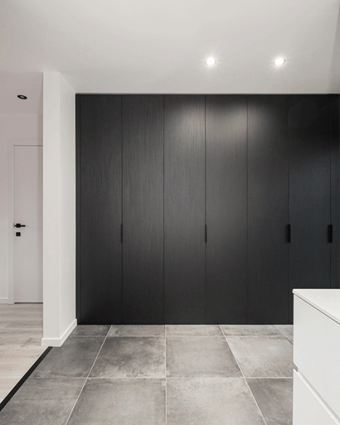 Armoire sur mesure en Elegant Black avec poignées Pure noires. L’armoire est fermée, et nous la voyons à quelques mètres de distance, ce qui permet de voir l’ensemble du meuble.