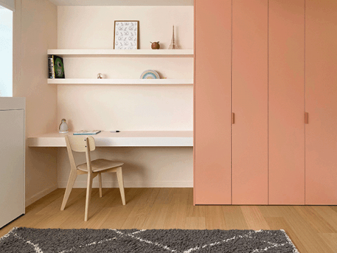 Op maat gemaakte kinderkamer kast in Dusty Coral met roze Tonton handgrepen. De kast staat aan de rechterkant van de foto, met links een bureau met een houten stoel.