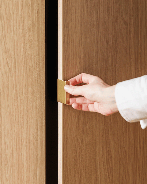 Detail shot van een mini pure messing handgreep op een maatkast in Atlas Oak. Rechts is er een hand die de deur van de kast opent.