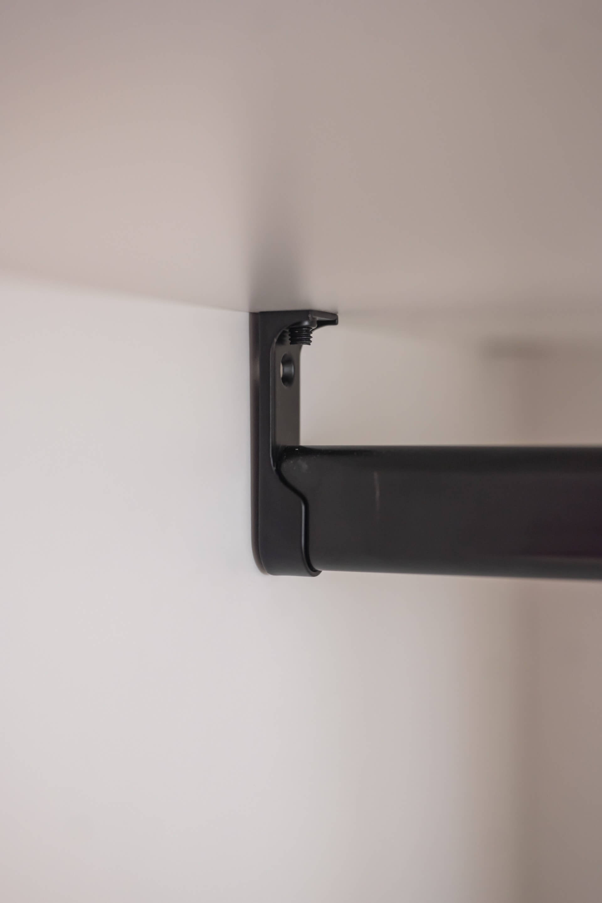 Plan rapproché d’une tringle de vêtements noire montée dans une armoire sur mesure blanche. Angle parfait de 90°.