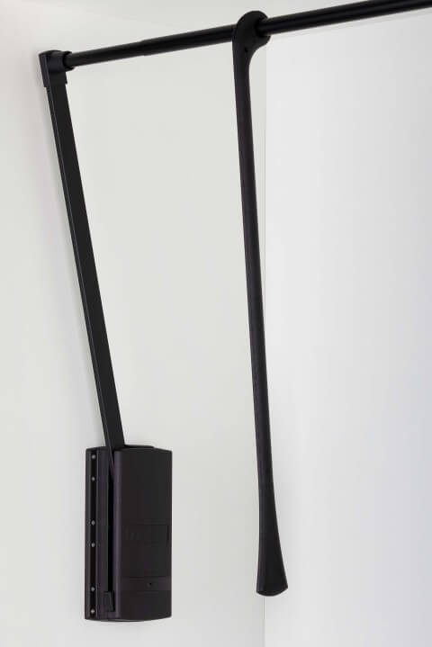 The image shows a sleek, modern design with metal arms and a housing finished entirely in matte black. The product is mounted inside a wardrobe and features a lifting mechanism that allows the clothing rail to be pulled down for easy access. The combination of sturdy construction and minimalist design ensures both functionality and a stylish appearance in wardrobe interiors.