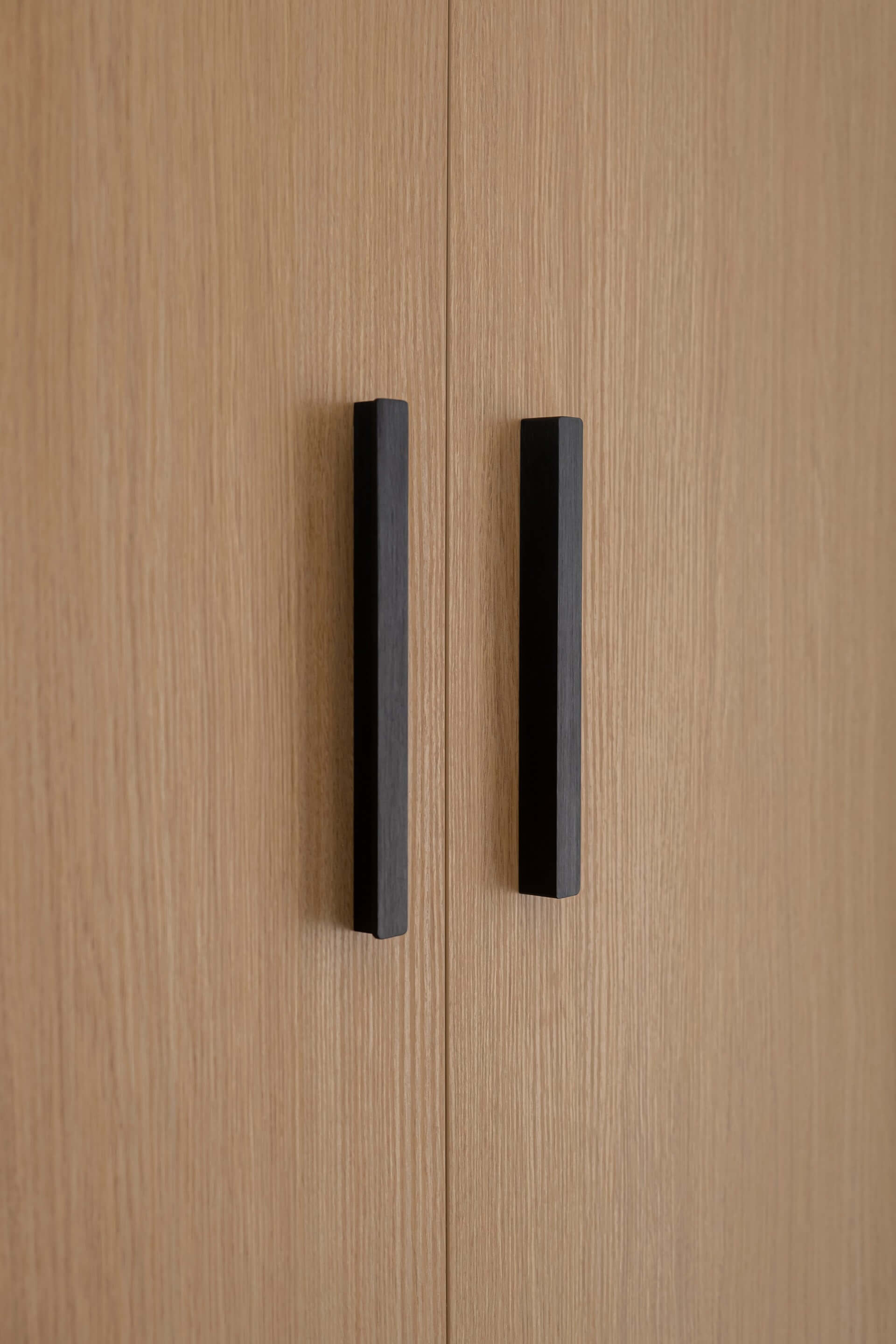 Gros plan sur les poignées noires d'un meuble sur mesure en Essential Oak Naturel.