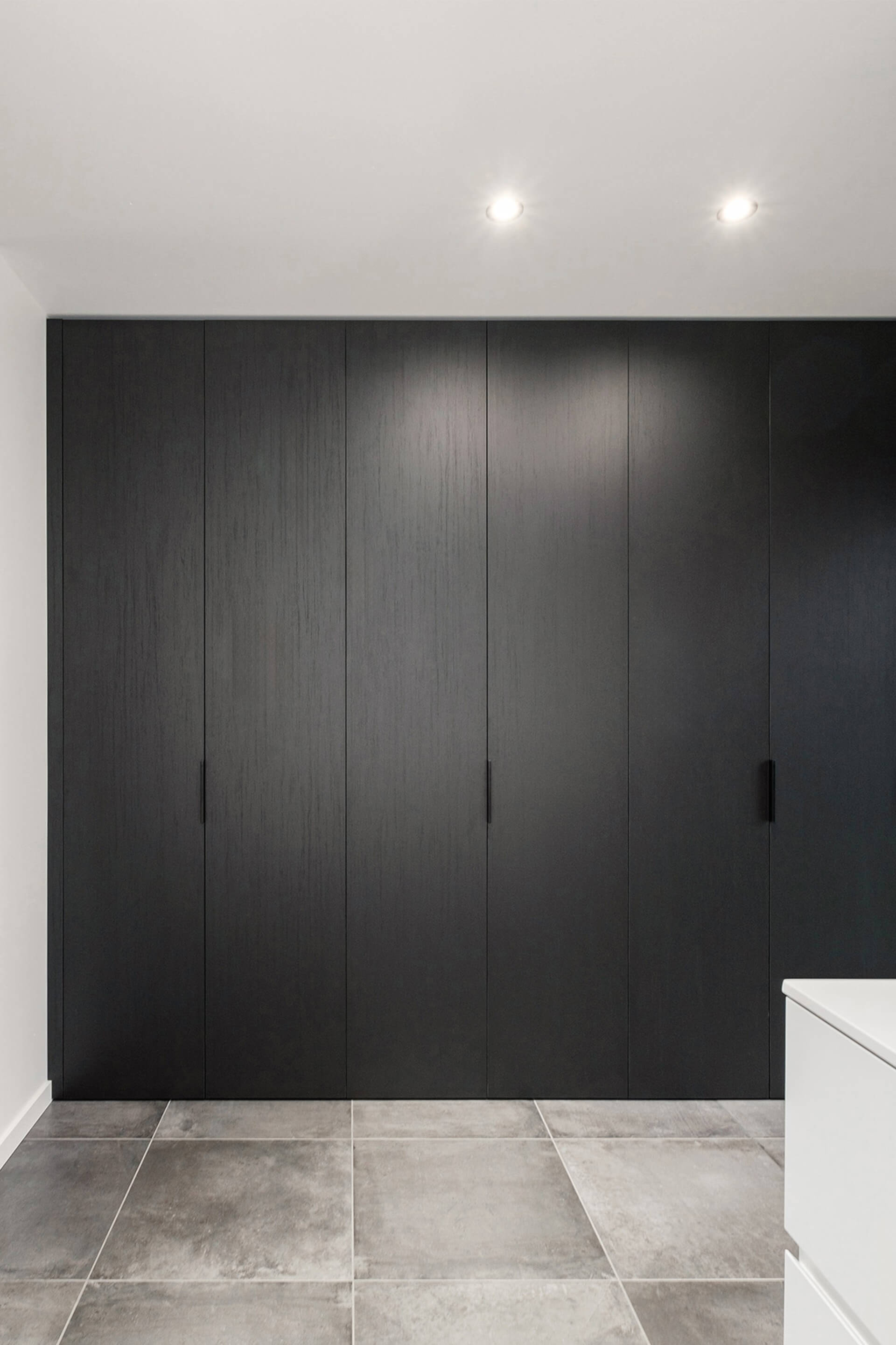 Op maat gemaakte kleerkast in Elegant Black met Pure handgrepen in zwart. De kast is gesloten, we kijken er van enkele meters op zodat we de hele dressingkast kunnen zien.