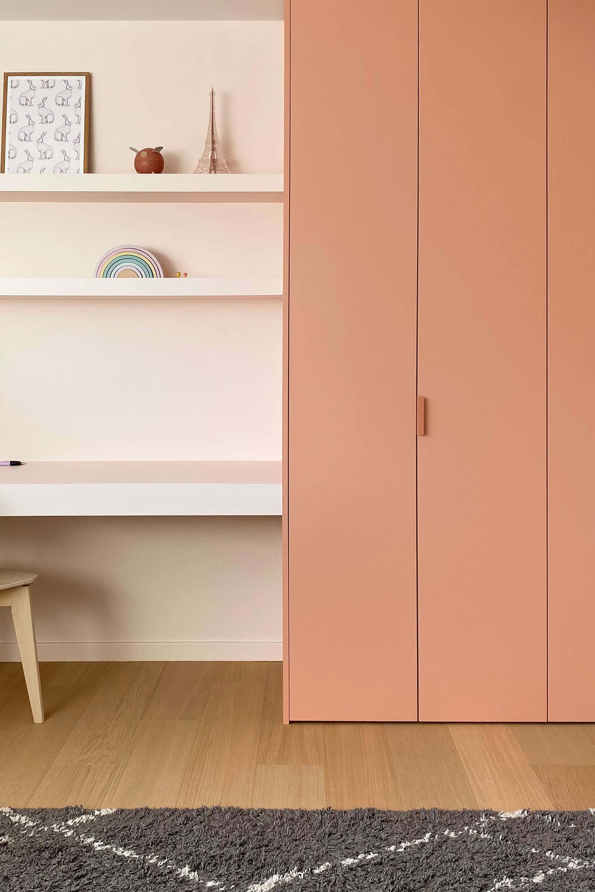Op maat gemaakte kinderkamer kast in Dusty Coral met roze Tonton handgrepen. De kast staat aan de rechterkant van de foto, met links een bureau met een houten stoel.