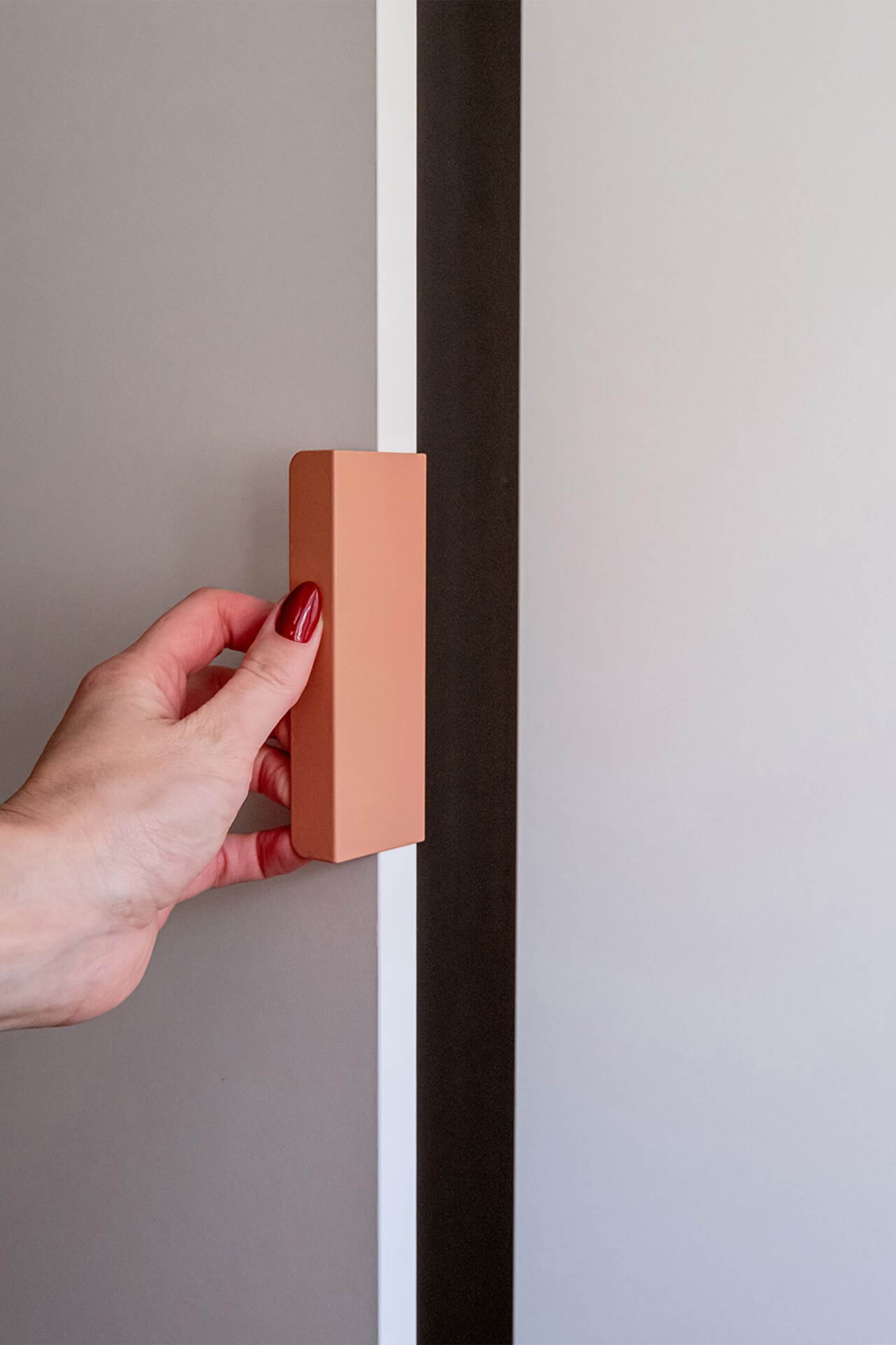 Detail shot van een roze Tonton handgreep die werd gemonteerd op een witte maatkast. Links in de foto zien we een hand de kast open doen.