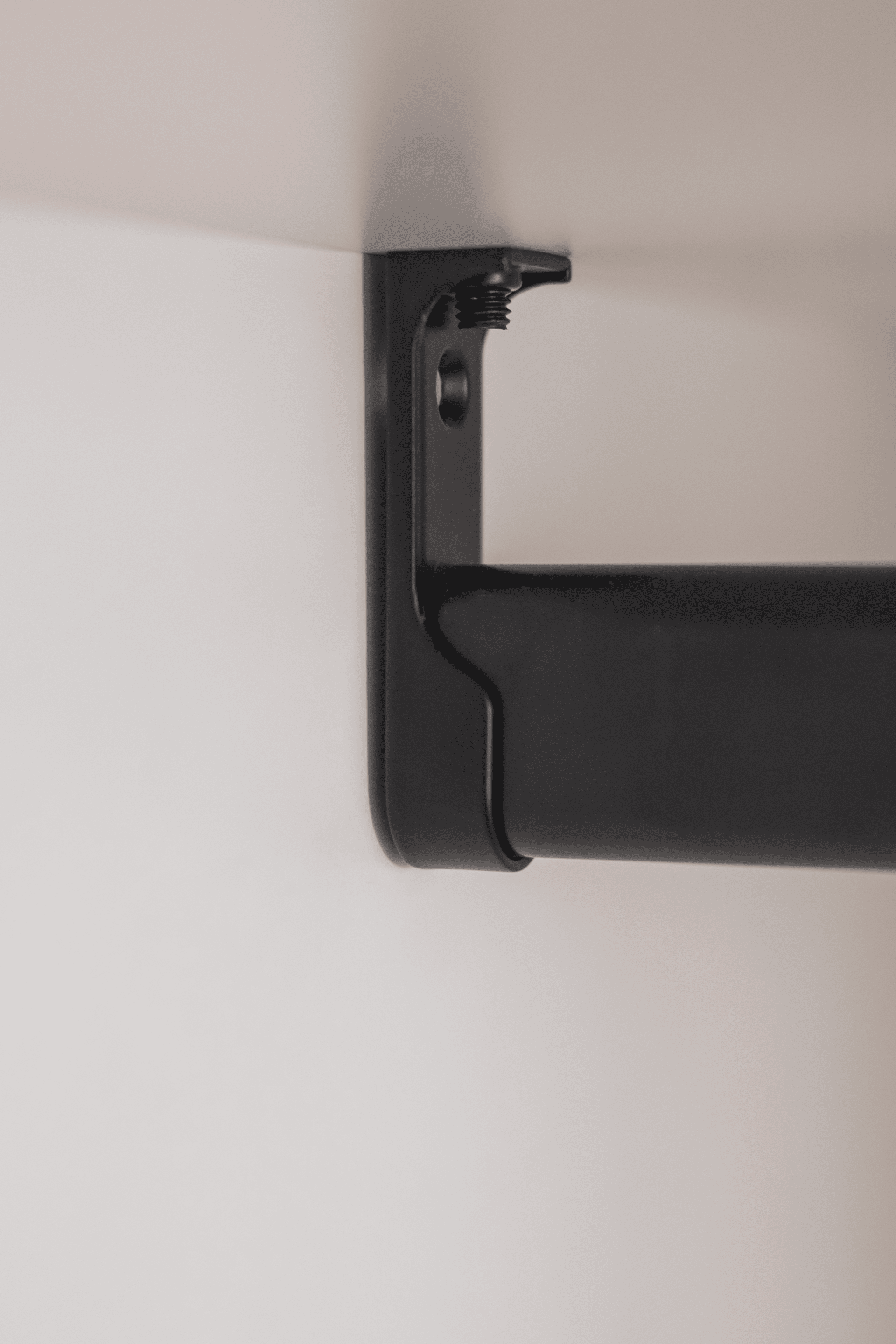 Detail shot van een zwarte kledijroede die gemonteerd is in een witte maatkast. Perfect hoek van 90°.